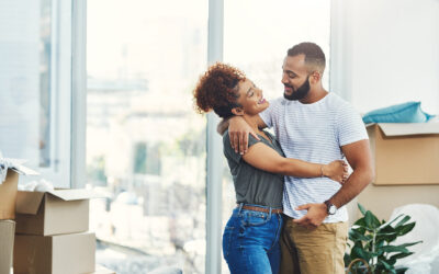 Smiling couple embracing in a bright room with moving boxes stacked behind them